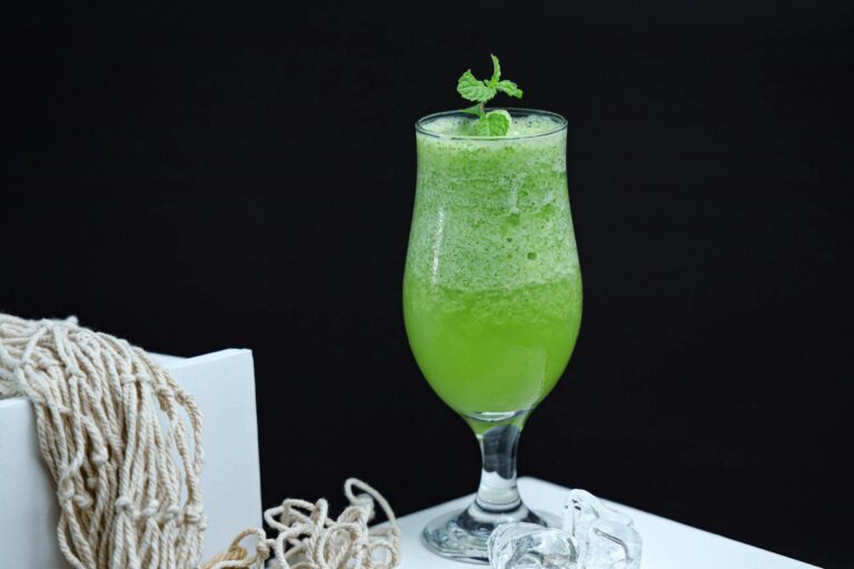 A fresh and healthy green smoothie in a glass with a mint garnish, placed against a dark background.